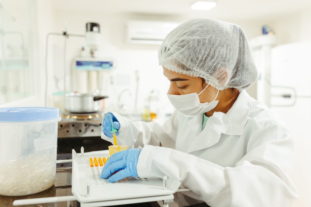 Pracownik laboratorium farmaceutycznego w stroju ochronnym napełniający kapsułki podczas produkcji suplementów diety